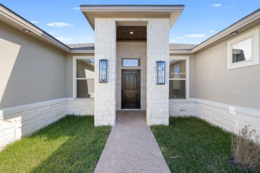 Doorway to property featuring stone siding, stucco siding, and a yard