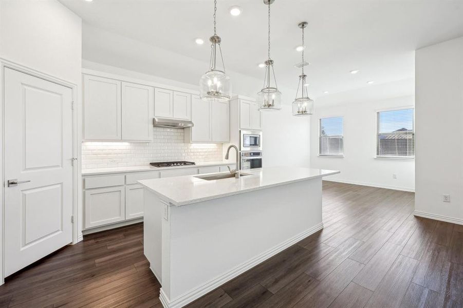 Kitchen with white cabinetry, a center island with sink, stainless steel appliances, and hanging light fixtures