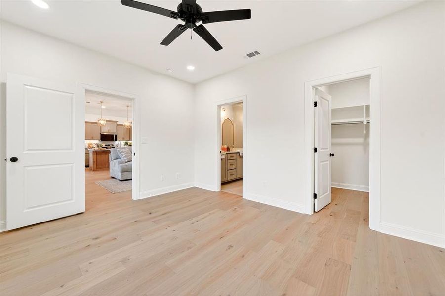Room featuring light wood-finish flooring, white walls, and a black ceiling fan with recessed lighting