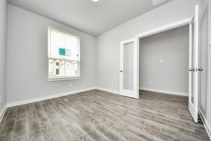 Experience the perfect blend of sophistication and warmth in this home office, boasting elegant wood-look tile flooring and flooded with natural light from expansive windows and French doors.