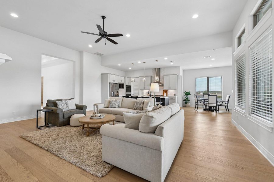 Open-concept living area featuring light wood-finish flooring, recessed lighting, a modern ceiling fan, and large windows with privacy blinds