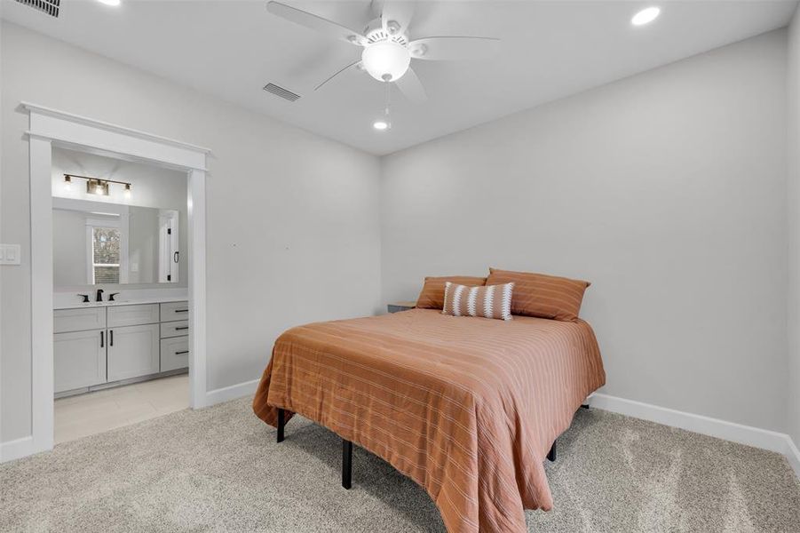 Bedroom featuring ceiling fan, sink, light carpet, and ensuite bath