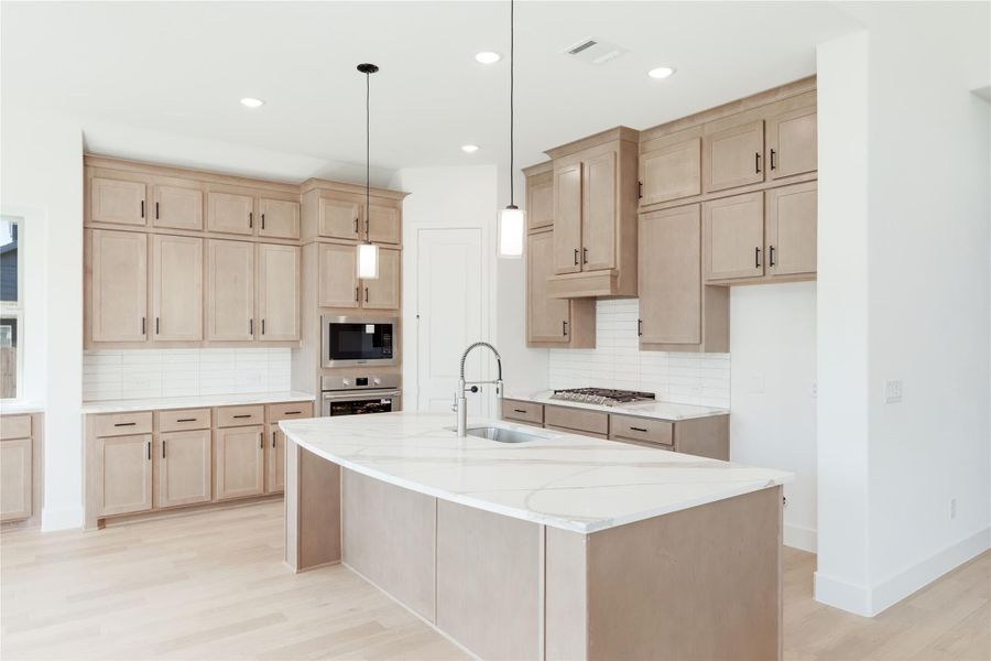 Kitchen with light wood cabinets, large island with quartz countertop, pendant lights, and stainless steel appliances