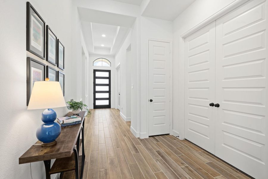 This photo shows a bright, welcoming entryway with wood tile flooring. A modern front door with frosted glass panels complements the space.