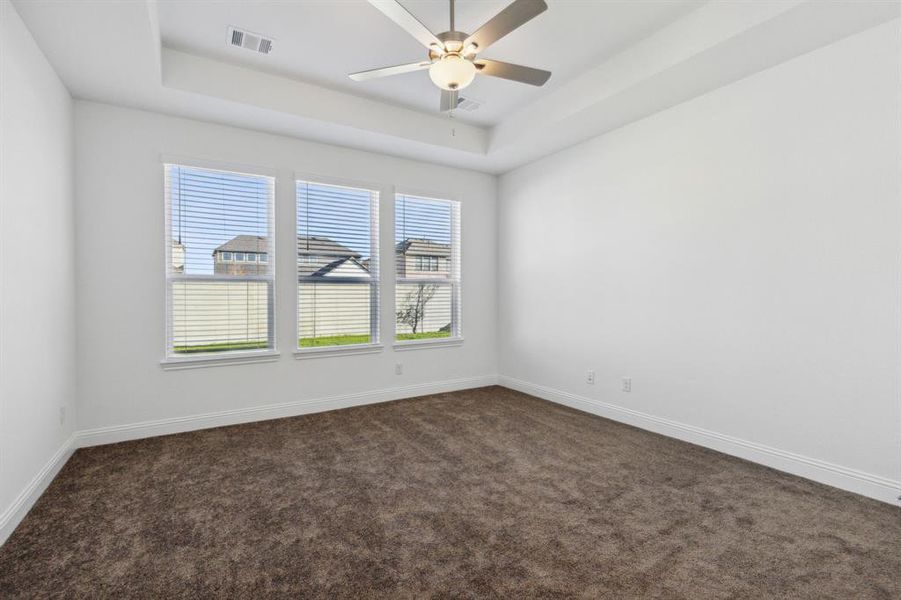 Unfurnished room featuring dark colored carpet, ceiling fan, and a tray ceiling