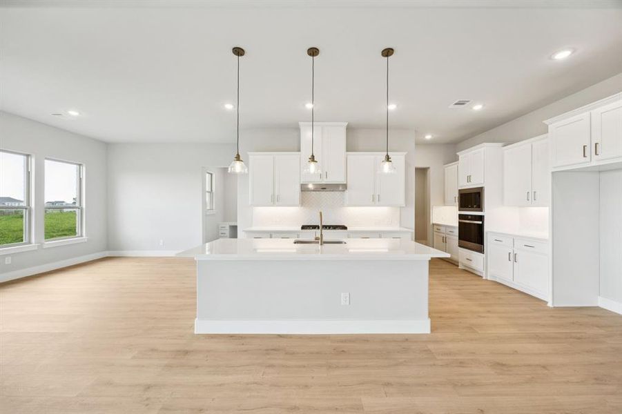 Kitchen featuring decorative backsplash, white cabinetry, a kitchen island with sink, decorative light fixtures, and recessed lighting