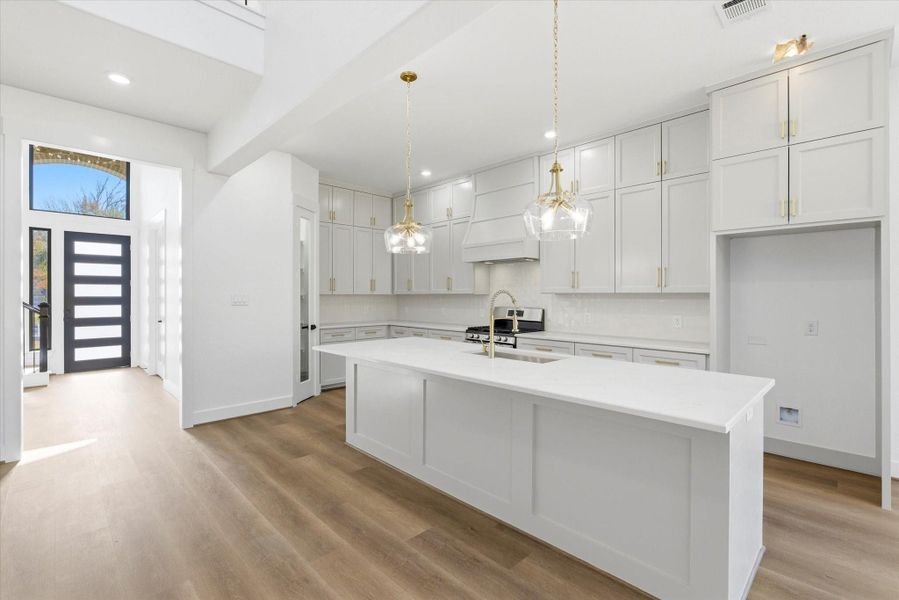 Just beyond the foyer, a stunning kitchen takes center stage, featuring an oversized island with additional seating, two statement pendant lights, a gas stove, and custom solid-wood cabinetry.