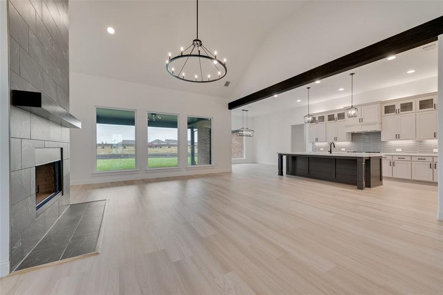 Unfurnished living room featuring beamed ceiling, light hardwood / wood-style flooring, an inviting chandelier, and a tile fireplace