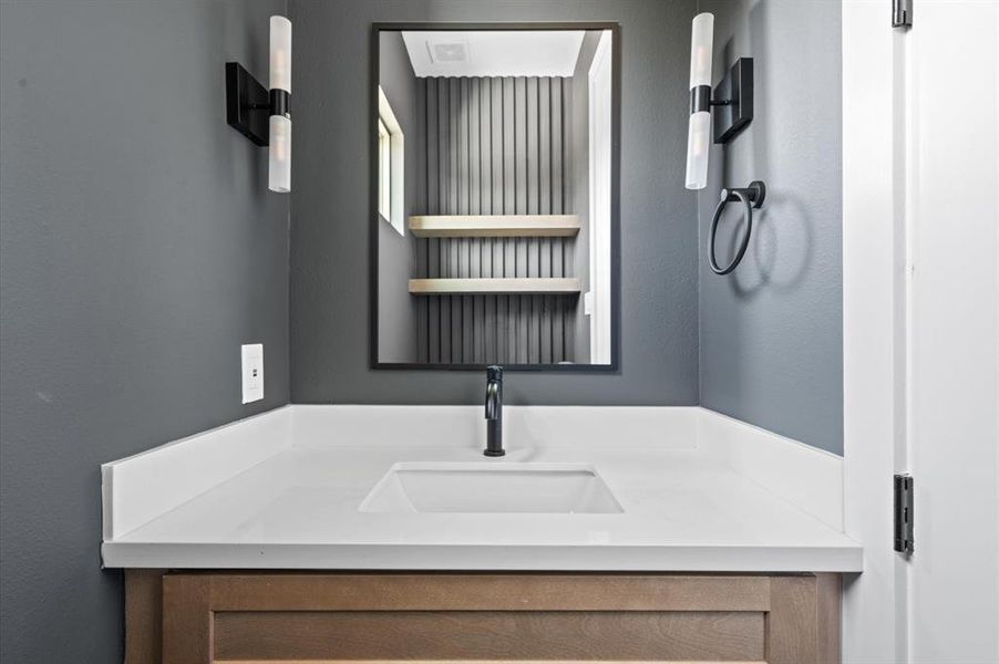 Second floor powder room tucked in near the stairs. Featuring a white Quartz countertop with wooden accents on the cabinetry.