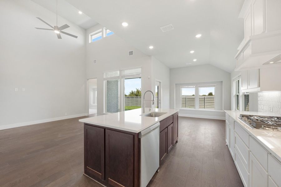 Open kitchen with dark wood island, white cabinets, vaulted ceiling, and hardwood floors open to living area Open kitchen with dark wood island, white cabinets, vaulted ceiling, and hardwood floors open to living area