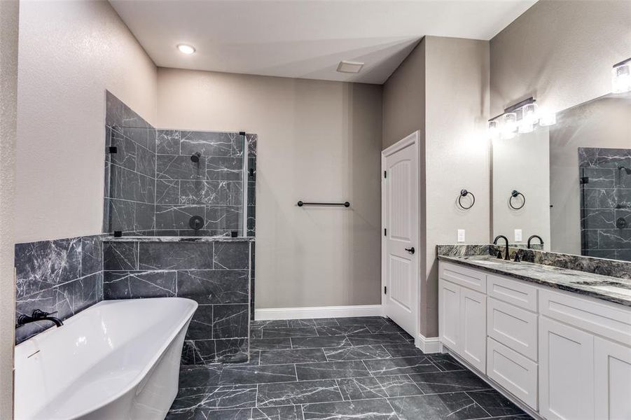 Bathroom with a freestanding bath, a marble finish shower, vanity, dark marble finish flooring, and tile walls Bathroom with a freestanding bath, a marble finish shower, vanity, dark marble finish flooring, and tile walls
