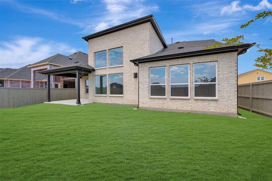 Spacious rear yard with a covered patio, expansive lawn, and light-colored brick exterior
