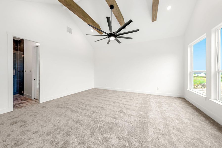 A spacious bedroom features vaulted ceilings with exposed wood beams and abundant natural light.