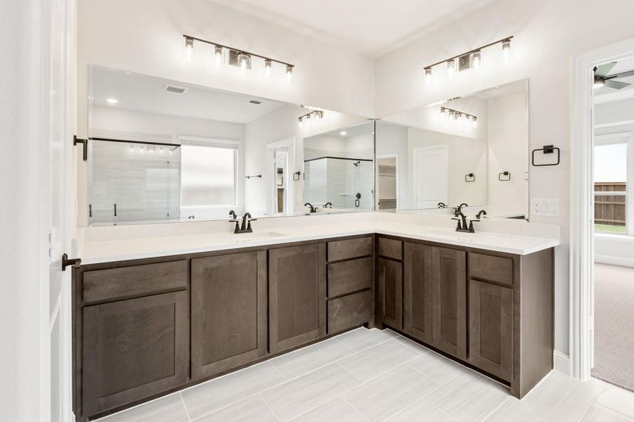 Master bathroom with L-shaped double vanity, dark wood cabinets, white countertops, and large mirrors with overhead lighting.