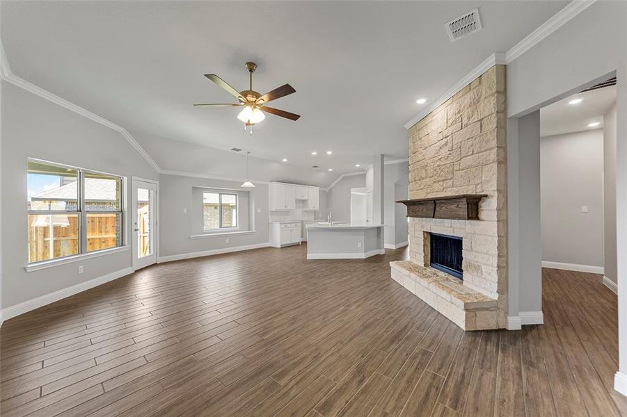 Unfurnished living room featuring a fireplace, ornamental molding, ceiling fan, and dark wood-type flooring