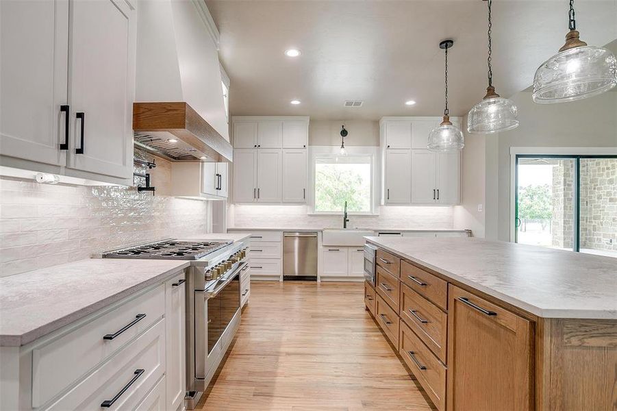 Kitchen featuring appliances with stainless steel finishes, premium range hood, a sink, light wood finished floors, and tasteful backsplash Kitchen featuring appliances with stainless steel finishes, premium range hood, a sink, light wood finished floors, and tasteful backsplash