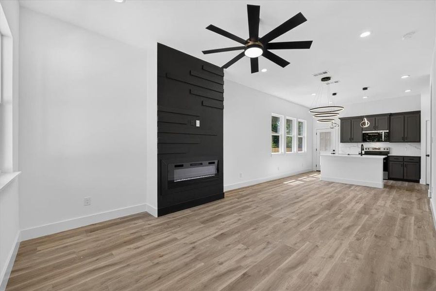 Open-concept living area featuring wood-finish flooring, a contemporary black accent wall with an integrated fireplace, and a modern ceiling fan Open-concept living area featuring wood-finish flooring, a contemporary black accent wall with an integrated fireplace, and a modern ceiling fan