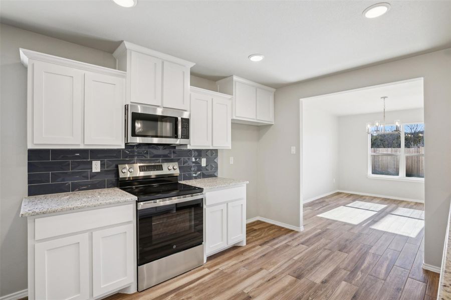 Kitchen featuring stainless steel appliances, backsplash, white cabinetry, light wood-style floors, and light stone countertops