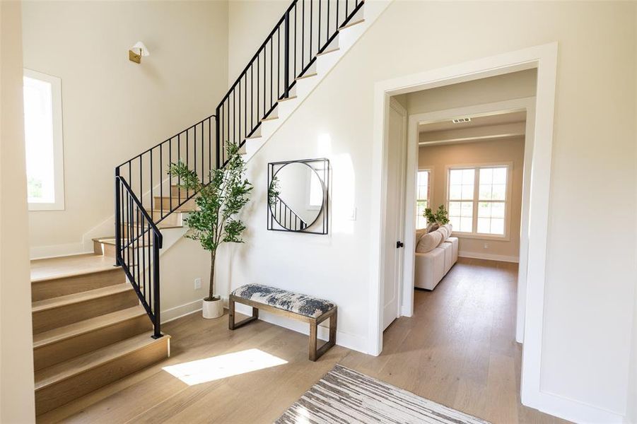 Gracious entryway featuring a wood-finish staircase with black metal balusters, high ceilings, and light-toned wood-finish flooring