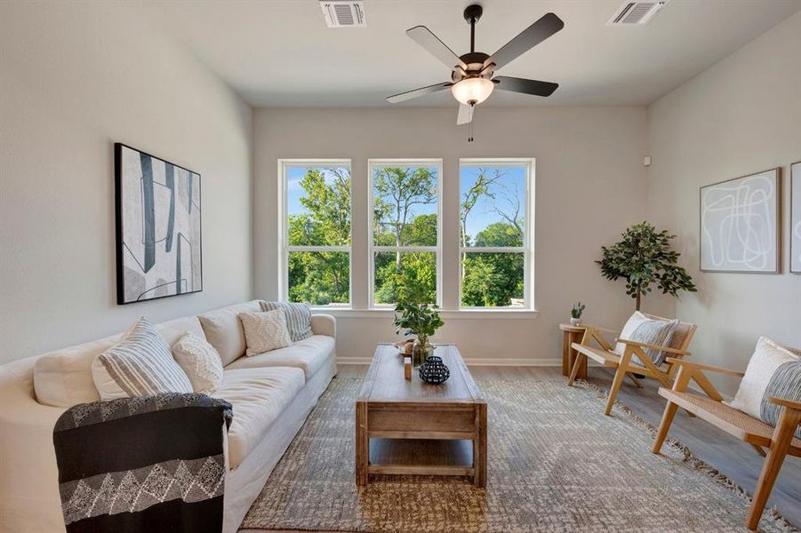 Living area featuring three large windows, a ceiling fan with integrated lighting, recessed lighting, wood-finish flooring, and light-toned walls