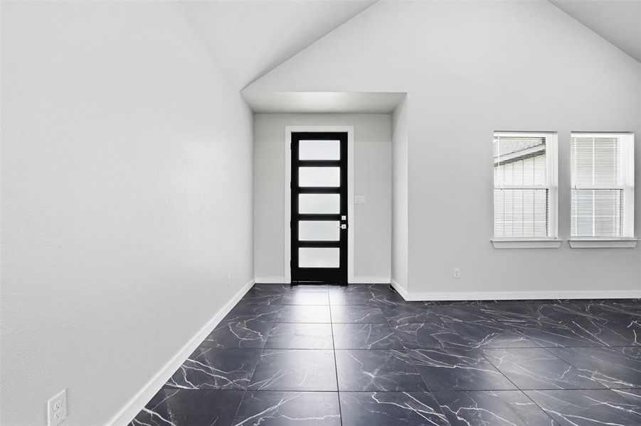 Entryway featuring a modern door with frosted glass panels, vaulted ceilings, two windows with blinds, and large format black tile flooring with white veining