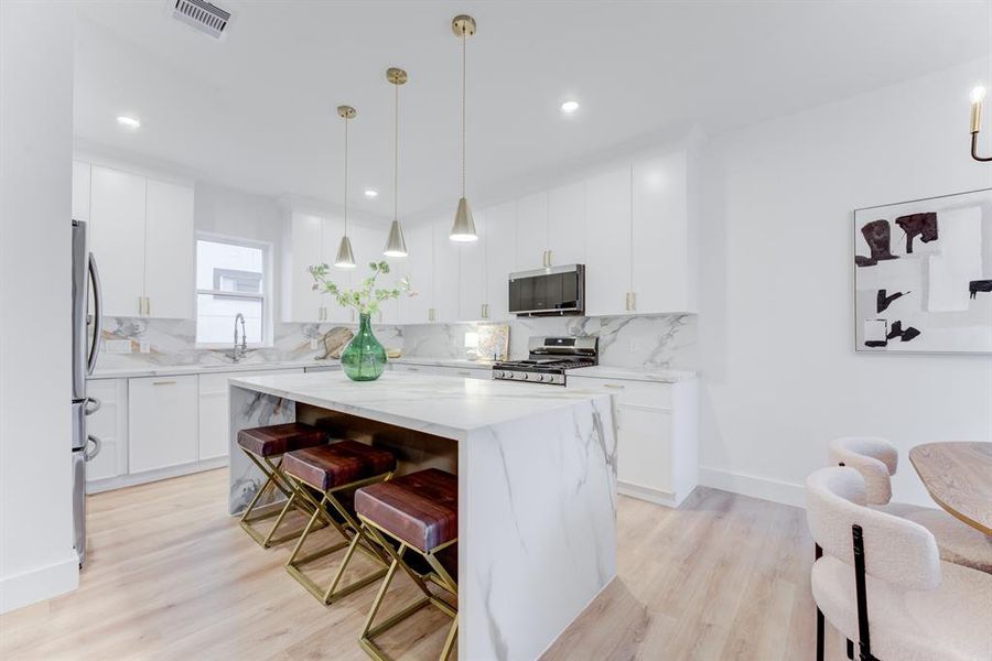 This stunning kitchen features gold hardware, quartz countertops, gas range, and stainless steel appliances. There is plenty of storage space in the cabinets.