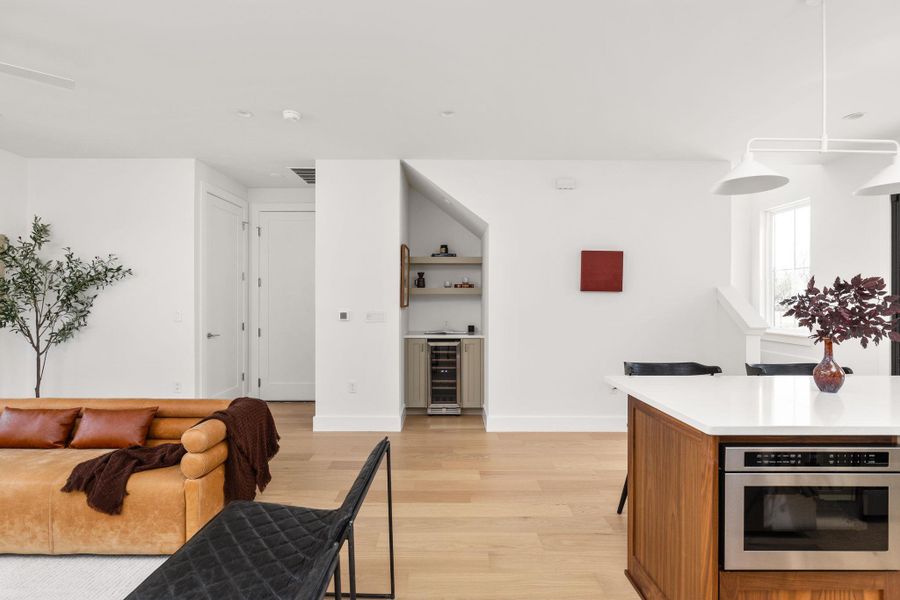 Kitchen with light wood-style flooring, a kitchen breakfast bar, wine cooler, pendant lighting, and stainless steel oven