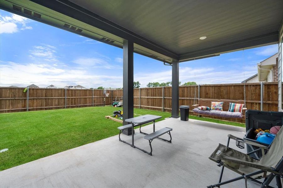 Covered patio with a concrete surface, featuring dark support columns and a ceiling fan