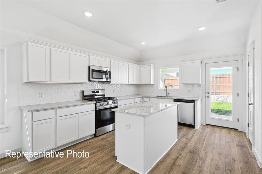 Bright kitchen featuring white cabinetry, granite countertops, stainless steel appliances, wood-finish flooring, and a white subway tile backsplash