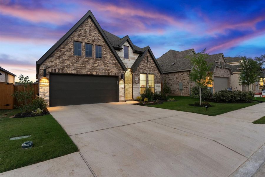 Brick and stone facade residence featuring a two-car garage, concrete driveway, and manicured front lawn