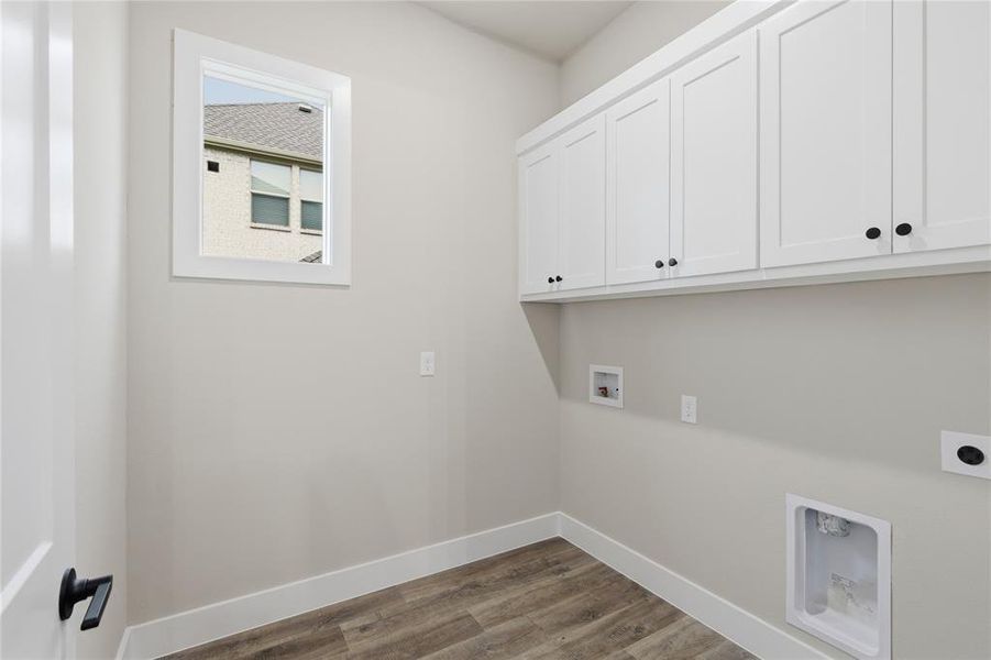 Utility room featuring white shaker-style cabinetry with black hardware, wood-finish flooring, and a single window with white trim Utility room featuring white shaker-style cabinetry with black hardware, wood-finish flooring, and a single window with white trim