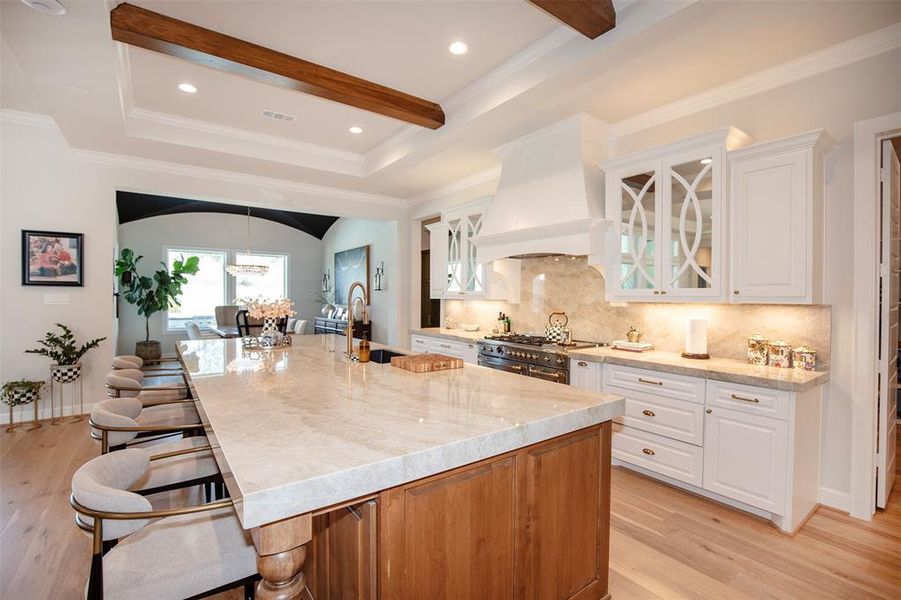 This photo showcases a spacious, elegant kitchen with a large marble island, wooden accents, and modern appliances. The white cabinetry and ample natural light create an inviting atmosphere, while the open layout connects to a dining area, enhancing the space's functionality and charm.