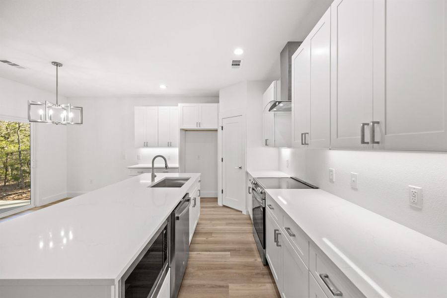 Kitchen with a center island with sink, stainless steel appliances, light stone counters, white cabinets, and light wood-style flooring