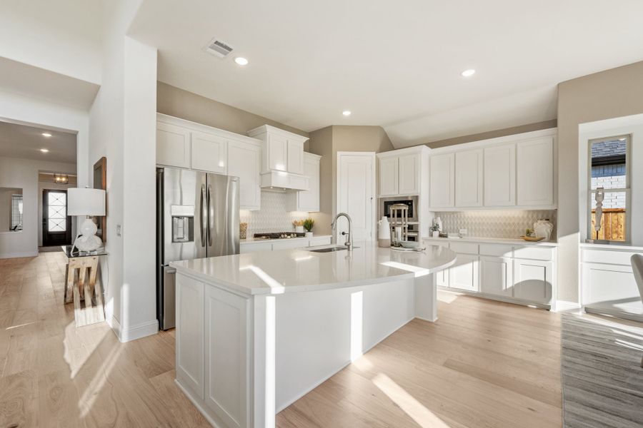 Open kitchen with white cabinets, large island, stainless steel refrigerator, and light hardwood floors