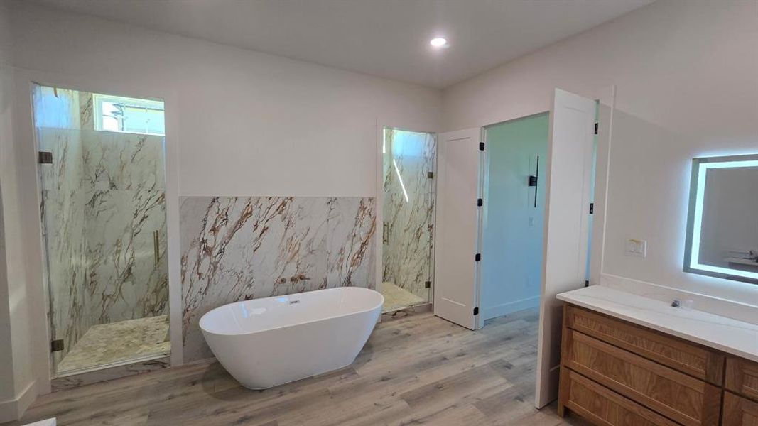 Full bathroom with a marble finish shower, a freestanding bath, tile walls, light wood-type flooring, and vanity
