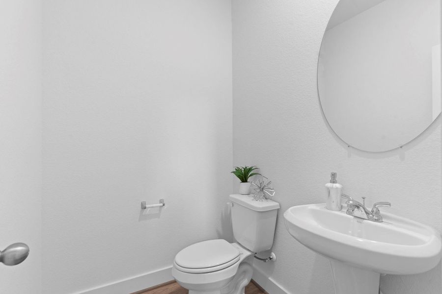 Stylish powder room on the first floor features a pedestal sink, elegant round mirror, and woodlike vinyl flooring—perfect for guests and conveniently located near the main living areas. **Image Representative of Plan Only and May Vary as Built**. Stylish powder room on the first floor features a pedestal sink, elegant round mirror, and woodlike vinyl flooring—perfect for guests and conveniently located near the main living areas. **Image Representative of Plan Only and May Vary as Built**.