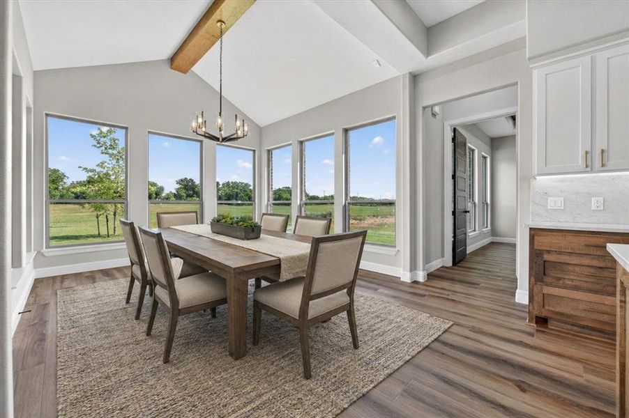 Dining area featuring a vaulted ceiling with exposed wood beam, multiple windows, wood-finish flooring, and a modern chandelier
