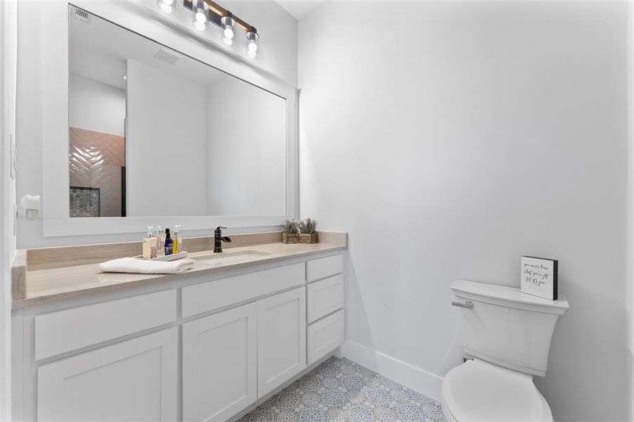 Bathroom featuring a white shaker-style vanity with ample storage, light-toned countertop, rectangular undermount sink, and matte black faucet