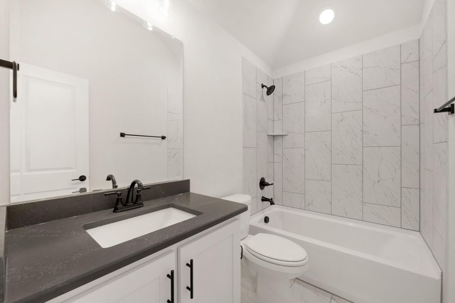 Bathroom with white cabinets, dark countertop, and tub-shower combo with marble-look tile surround