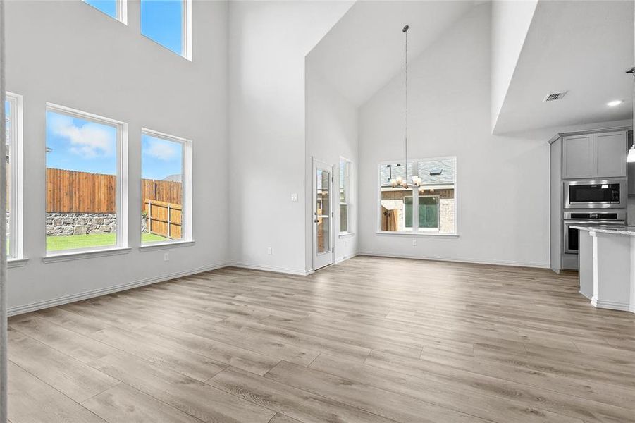 Unfurnished living room featuring a towering ceiling, plenty of natural light, a chandelier, and light wood-style flooring Unfurnished living room featuring a towering ceiling, plenty of natural light, a chandelier, and light wood-style flooring