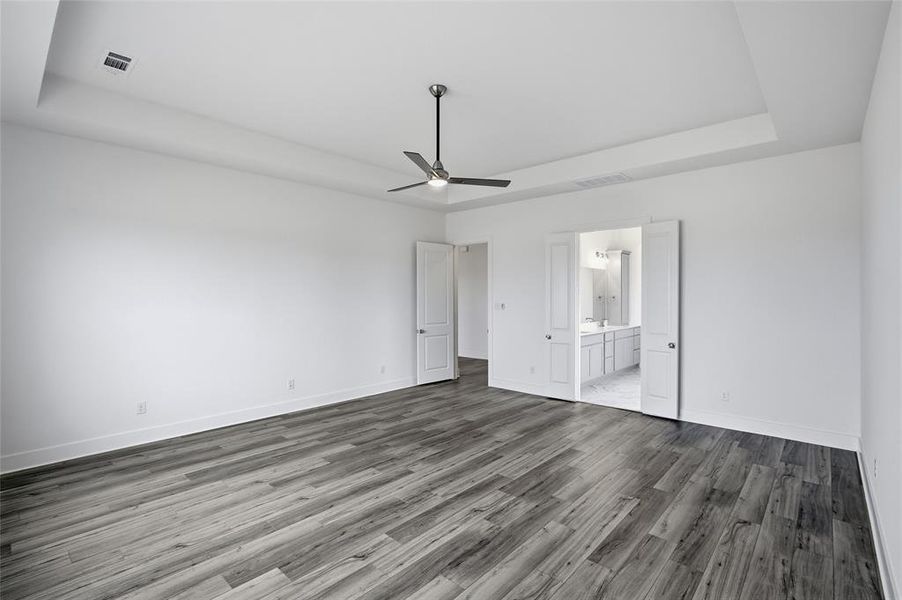 Unfurnished bedroom featuring a tray ceiling, ceiling fan, wood finished floors, and connected bathroom