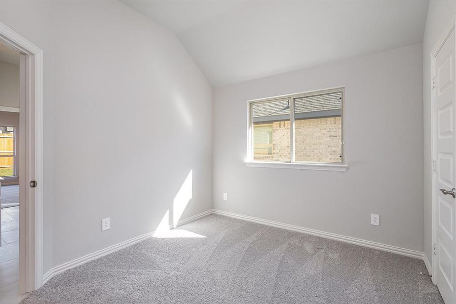 Carpeted spare room featuring vaulted ceiling