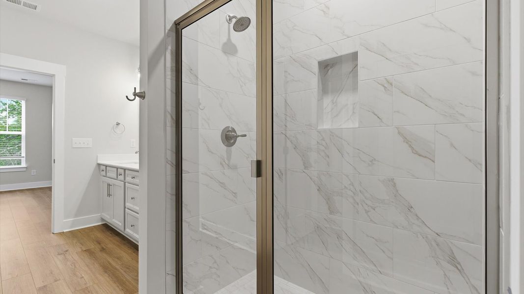Notable primary bath featuring a walk-in shower, hardwood floors, and tasteful design touches throughout at Village at Midway Notable primary bath featuring a walk-in shower, hardwood floors, and tasteful design touches throughout at Village at Midway