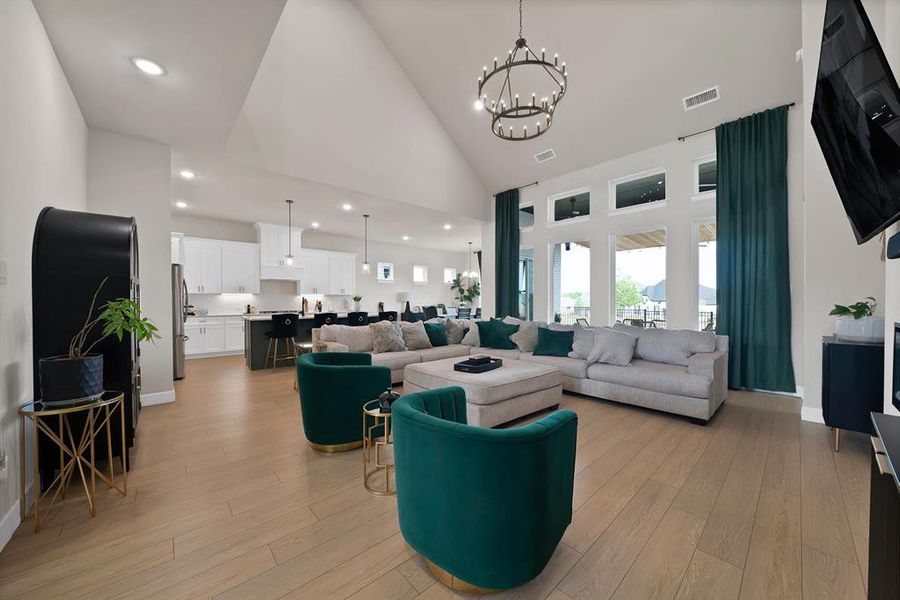 Spacious open-concept living area featuring high vaulted ceilings, light wood-finish flooring, and large windows with transom details Spacious open-concept living area featuring high vaulted ceilings, light wood-finish flooring, and large windows with transom details