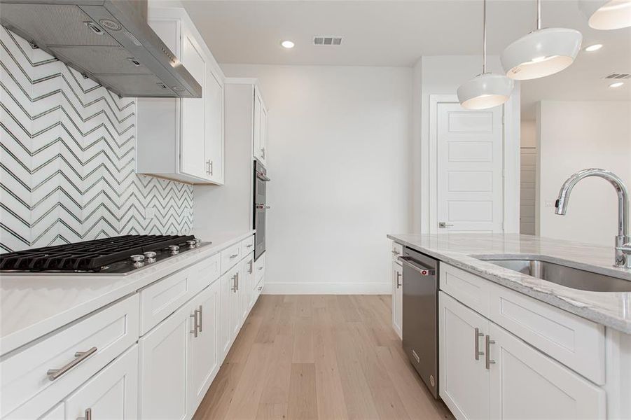 Kitchen featuring appliances with stainless steel finishes, white cabinets, light wood-type flooring, sink, and wall chimney exhaust hood