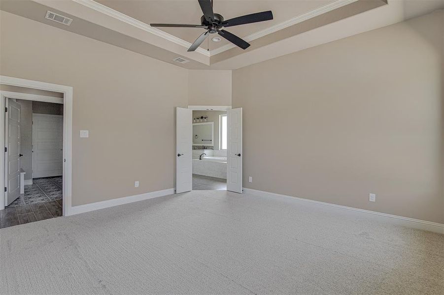 Unfurnished bedroom featuring ceiling fan, ensuite bathroom, ornamental molding, and a raised ceiling