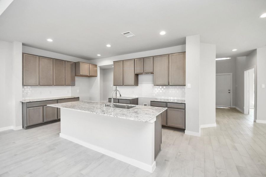 Discover another perspective of this stunning kitchen, sleek back splash, single basin sink, and generously appointed with an abundance of counter space. Sample photo of completed home with similar floor plan. Actual colors and selections may vary.