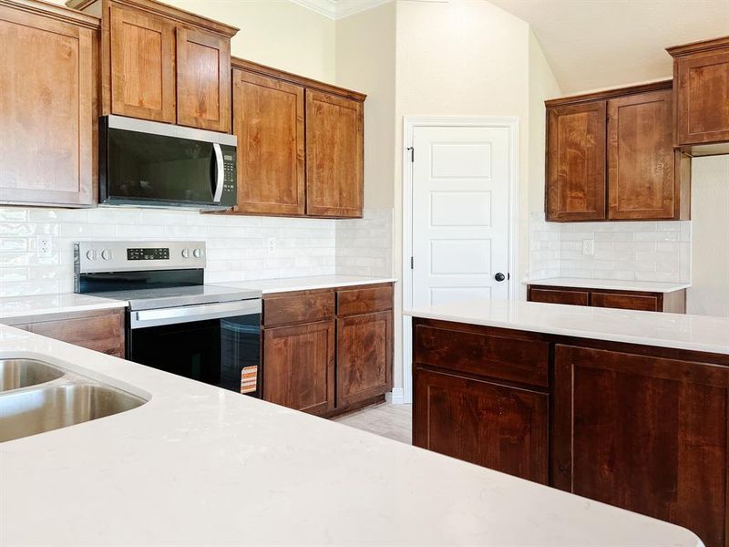 Kitchen with tasteful backsplash, stainless steel appliances, light stone countertops, brown cabinets, and crown molding Kitchen with tasteful backsplash, stainless steel appliances, light stone countertops, brown cabinets, and crown molding