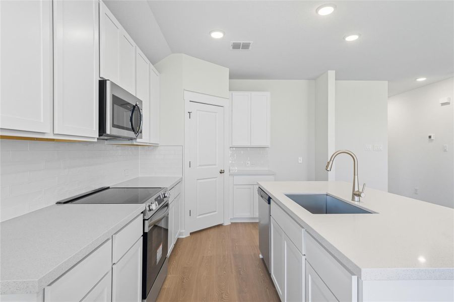 Kitchen with stainless steel appliances, light wood-style floors, a center island with sink, recessed lighting, and tasteful backsplash