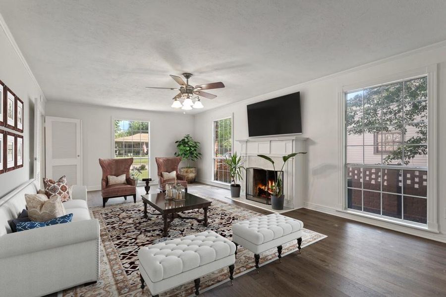 Living area featuring a warm lit fireplace, wood finished floors, a ceiling fan, ornamental molding, and baseboards